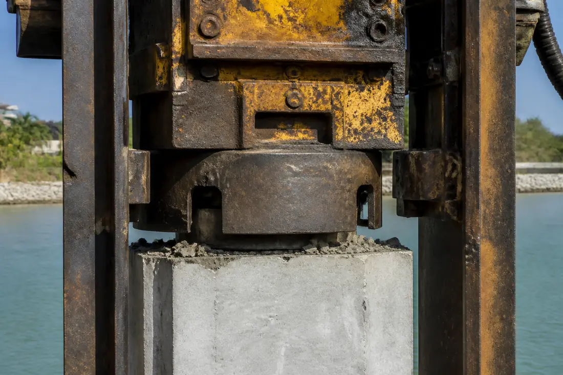 The head of a pile driving hammer seated on the top of a concrete pile
