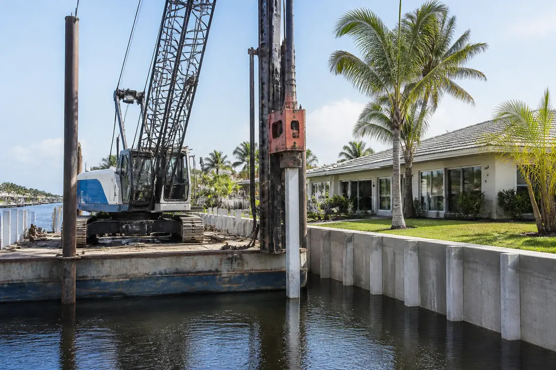 A barge-mounted pile driving rig working beside a residential canal seawall in Southwest Florida