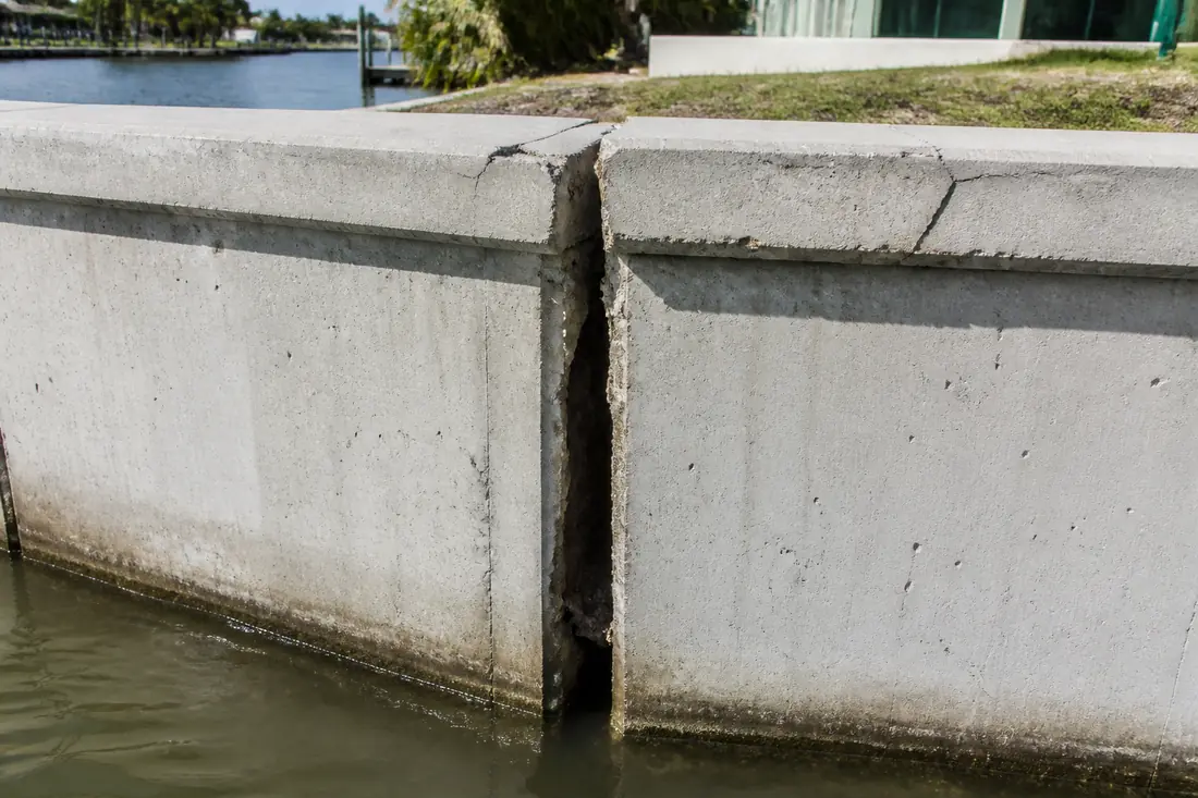 An open vertical joint between two seawall panels below a cracked concrete cap