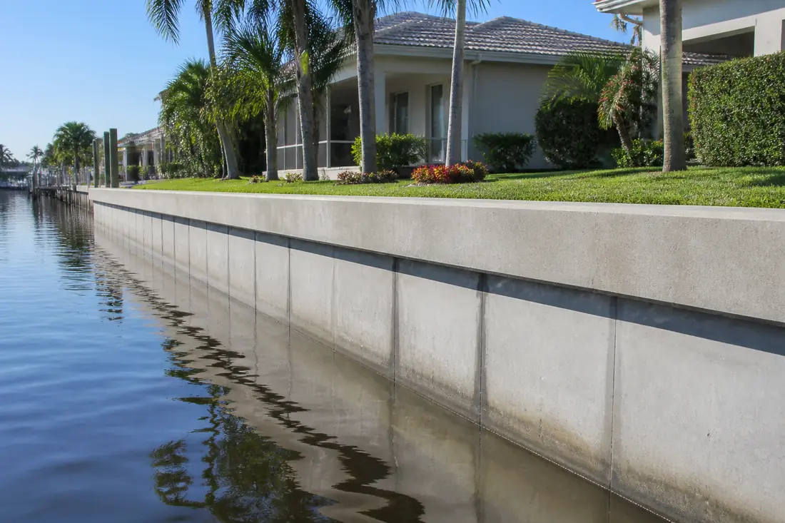 A concrete seawall running along a residential canal in Port Charlotte with houses and docks behind it